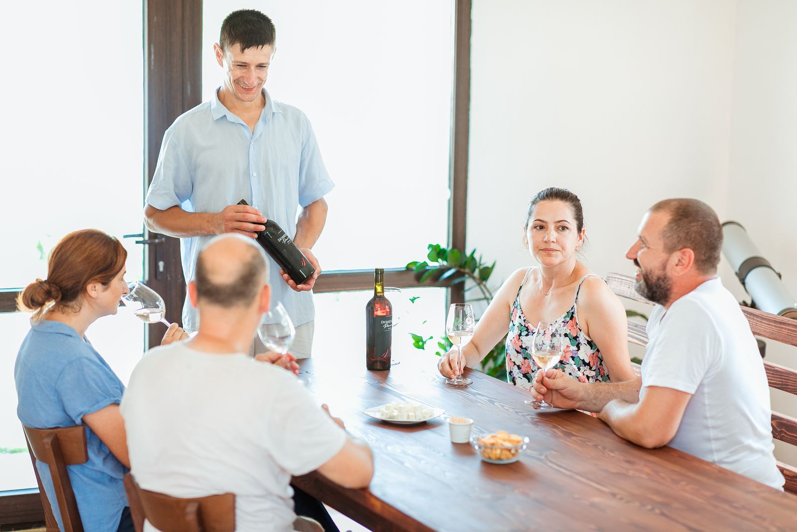 Oaspeți la o degustare de vin local, serviți de gazdă la o masă lungă
