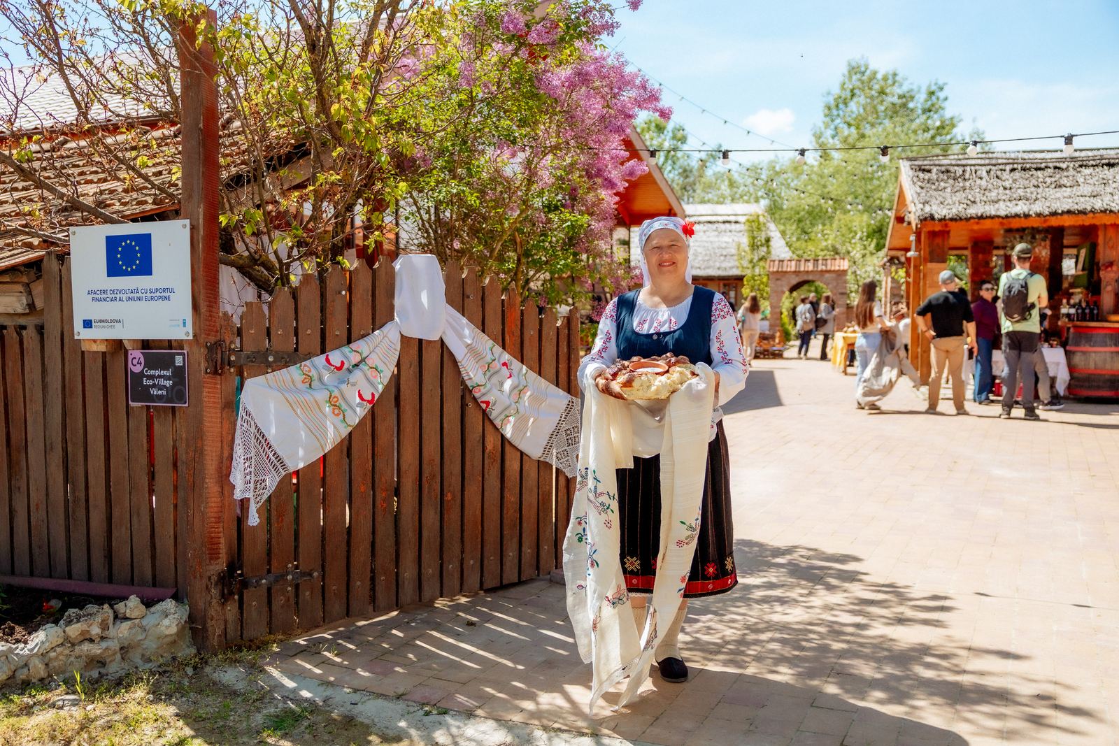 Gazdă în costum popular întâmpinând oaspeții cu pâine și sare la Complexul Eco-Village din Văleni, afacere dezvoltată cu sprijinul Uniunii Europene
