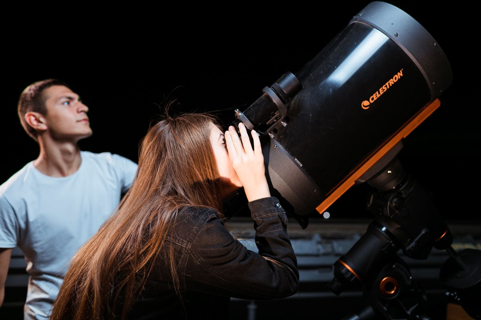 Doi tineri la o seară de observații astronomice, privind printr-un telescop